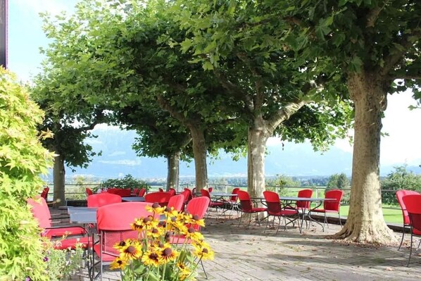 Un espace extérieur aménagé avec des chaises et des tables rouges, entouré d’arbres et offrant une vue sur le paysage.