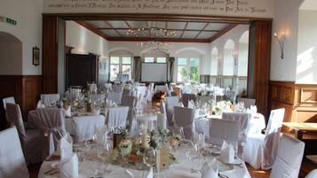 Une salle de banquet avec des tables rondes dressées pour un événement formel, agrémentée de nappes blanches, de verres et de compositions florales.