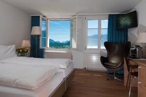 A hotel room with a bed, a desk, a chair, a TV, and a window with a mountain view.