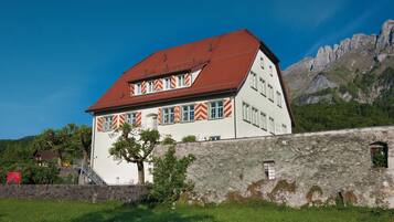 A traditional building with a red roof and striped window sills, set against a mountainous backdrop.