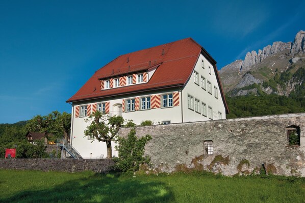 A traditional building with a red roof and striped window sills, set against a mountainous backdrop.