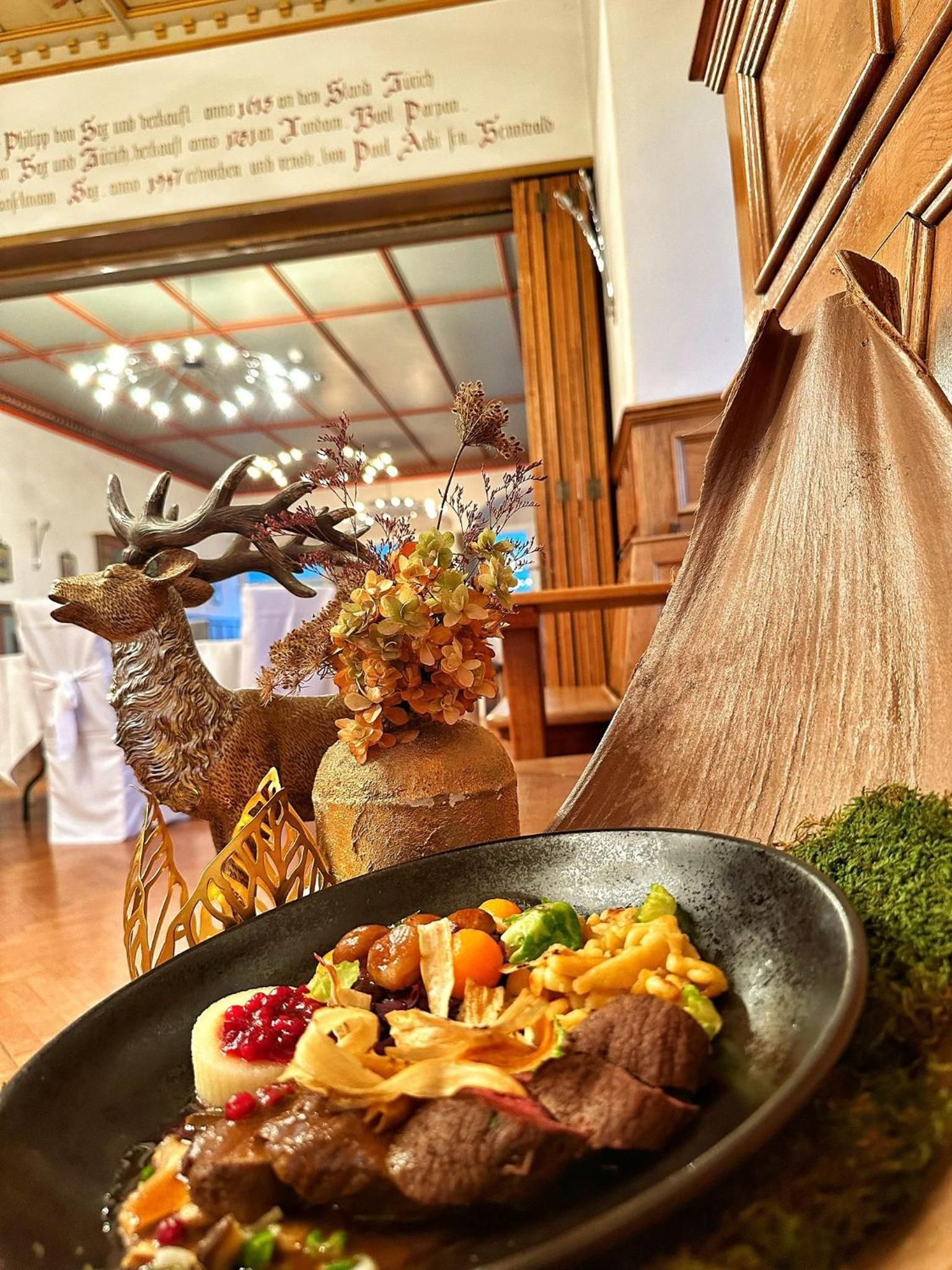 A dining table with a plate of food, a decorative deer head, and a wooden structure.