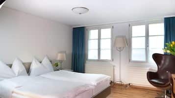 A hotel room with a bed, a chair, a desk, and a window with curtains.