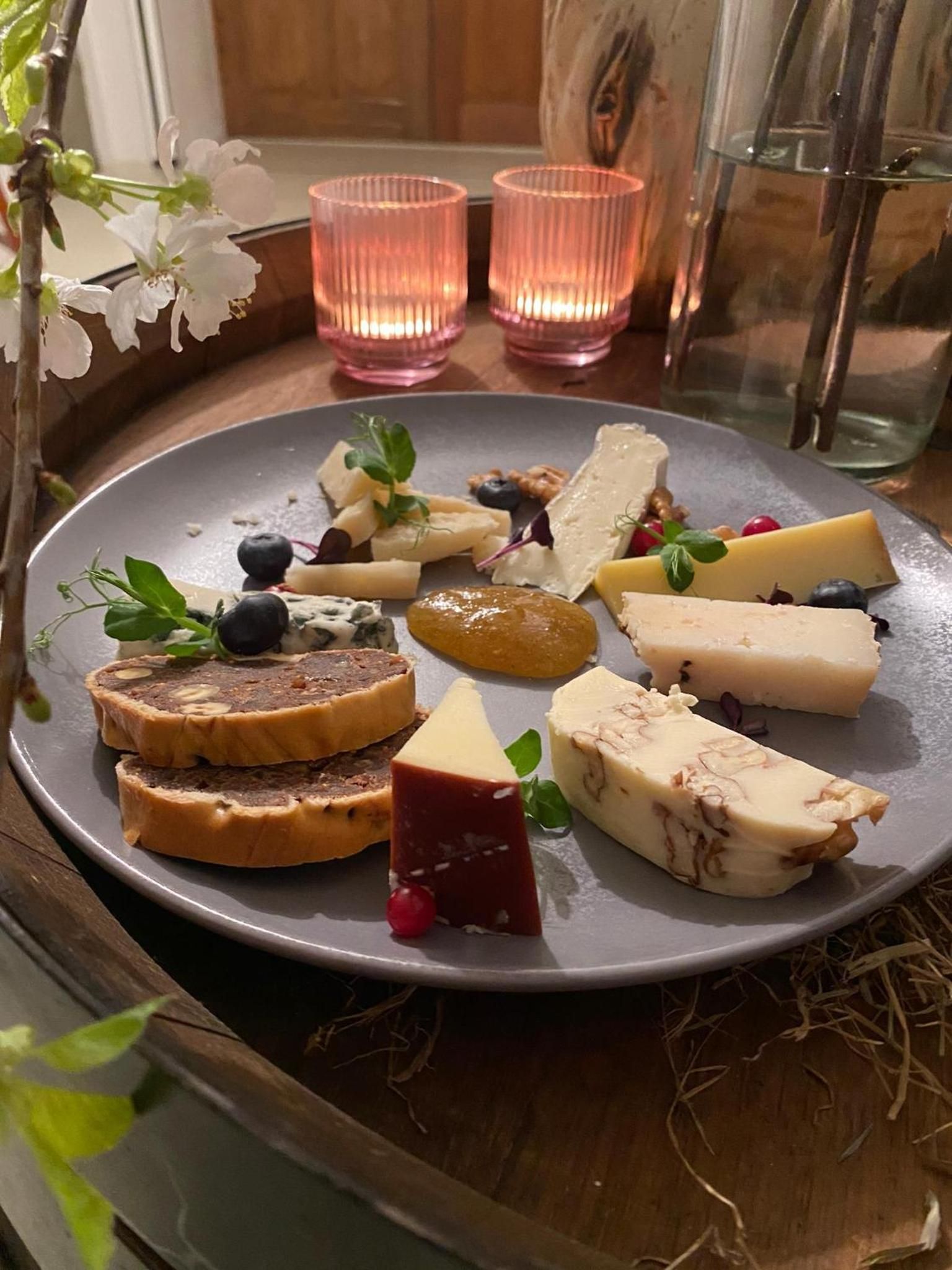 A plate of assorted cheeses and fruits on a table with candles.