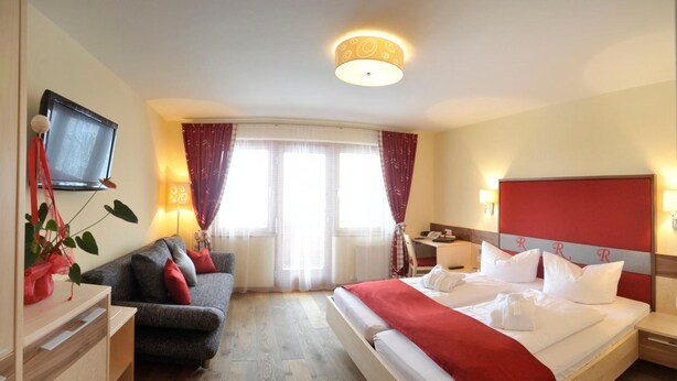 A hotel room with a bed, a desk, a sofa, and a television. - Rösslhof (Ramsau am Dachstein)