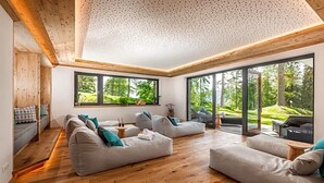 A modern living room with a wooden floor, large windows, and a view of greenery. - Rösslhof (Ramsau am Dachstein)