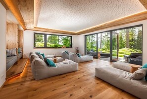 A modern living room with a wooden floor, large windows, and a view of greenery. - Rösslhof (Ramsau am Dachstein)