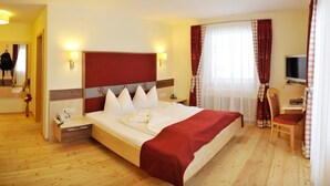 A hotel room with a bed, bedside tables, a desk with a chair, a television, and a window with curtains. - Rösslhof (Ramsau am Dachstein)