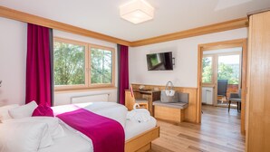 A hotel room with a bed, a desk, a chair, a TV, and a view of the outdoors. - Rösslhof (Ramsau am Dachstein)