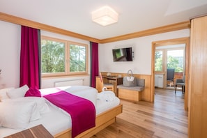A hotel room with a bed, a desk, a chair, a TV, and a view of the outdoors. - Rösslhof (Ramsau am Dachstein)