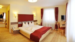 A hotel room with a large bed, a desk with a chair, a television, and a window with curtains. - Rösslhof (Ramsau am Dachstein)