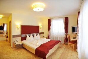 A hotel room with a large bed, a desk with a chair, a television, and a window with curtains. - Rösslhof (Ramsau am Dachstein)