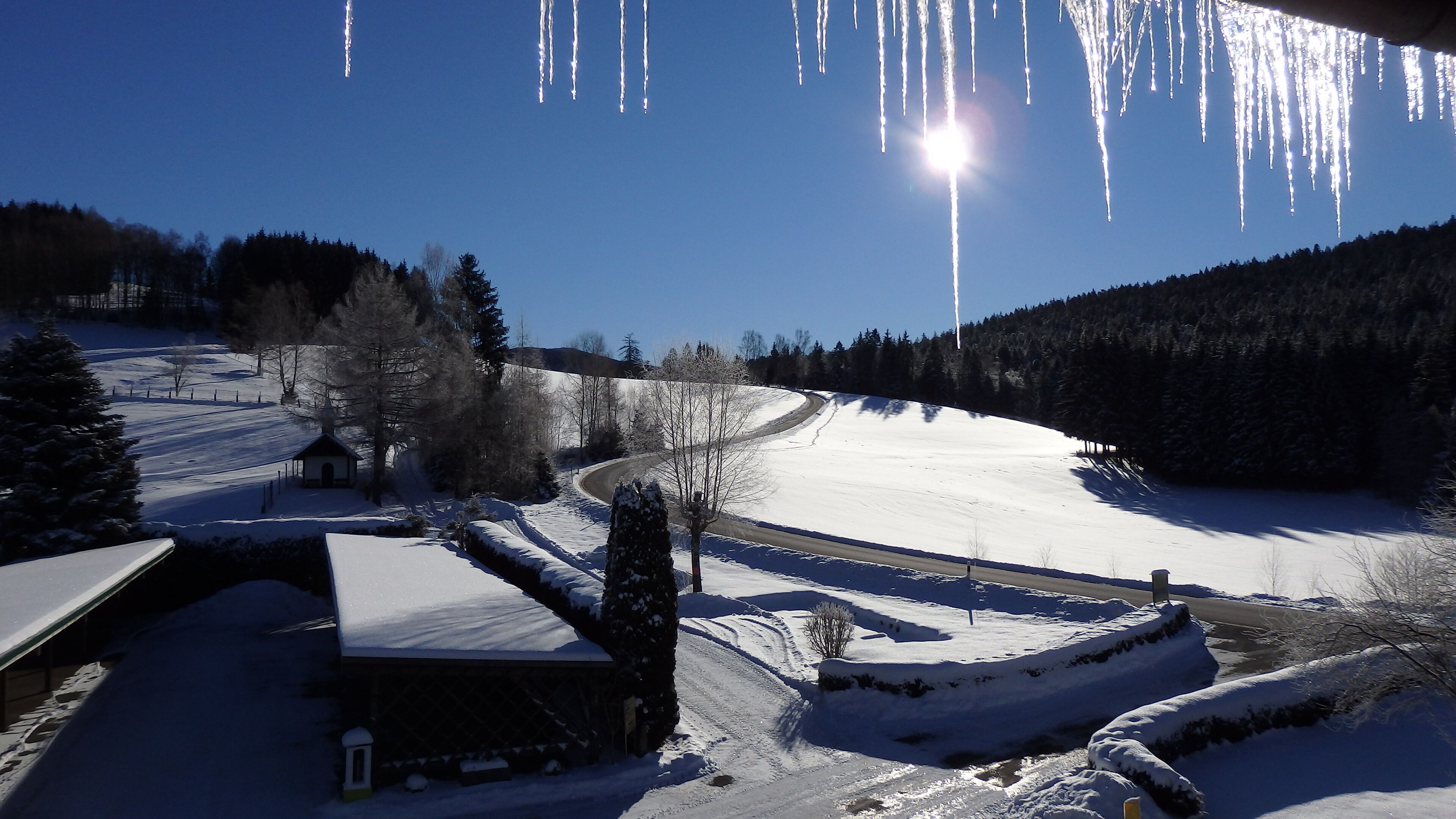 A snow-covered landscape with a clear sky, a winding road, and a small building with a snow-covered roof.