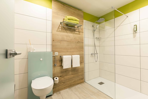 A modern bathroom with a wooden accent wall, a glass shower enclosure, and a toilet with a paper towel dispenser. - Garni GrünWies - Adults Only (Lohberg)