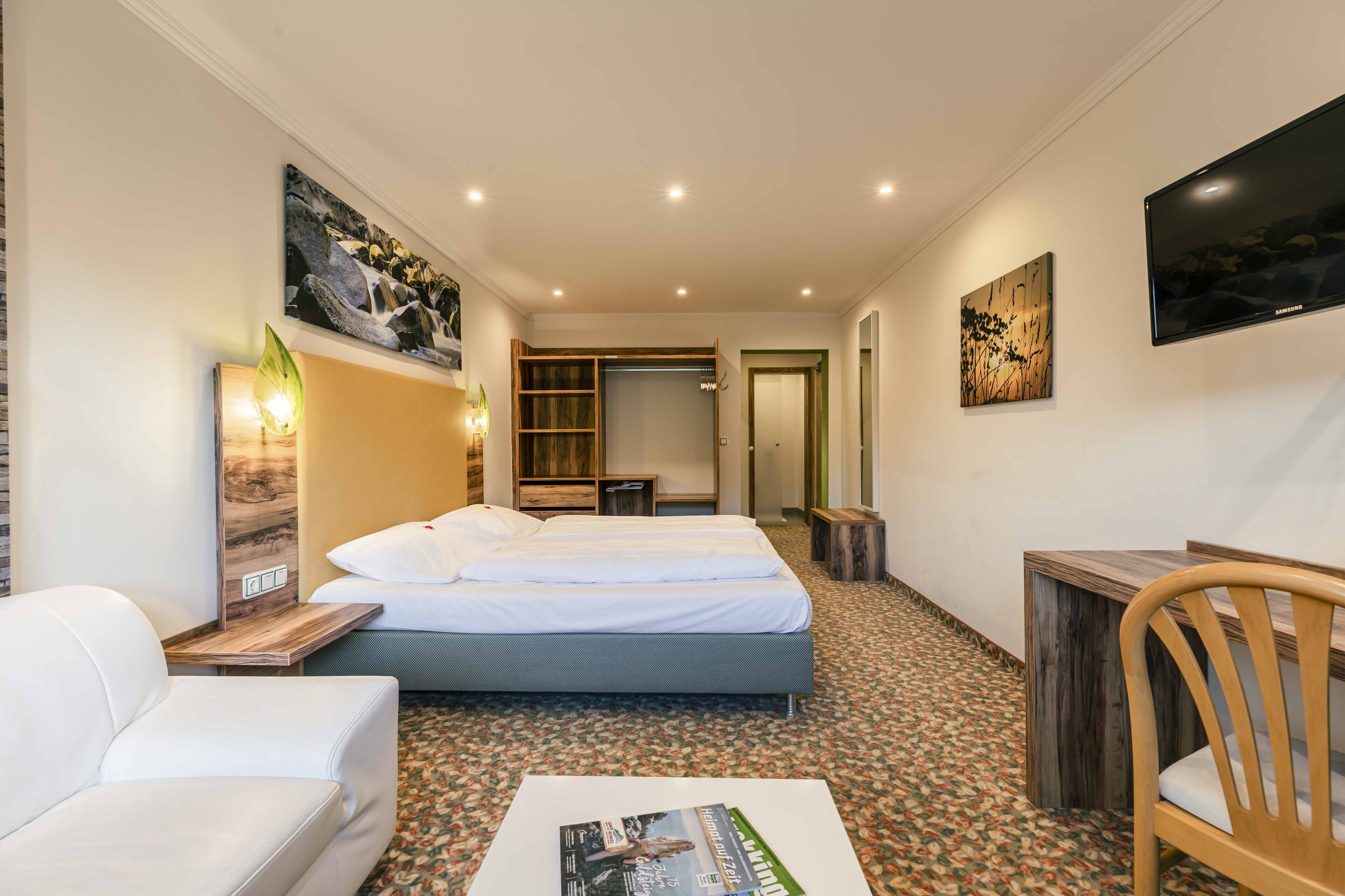 A hotel room with a bed, a desk, a chair, a TV, and artwork on the walls.