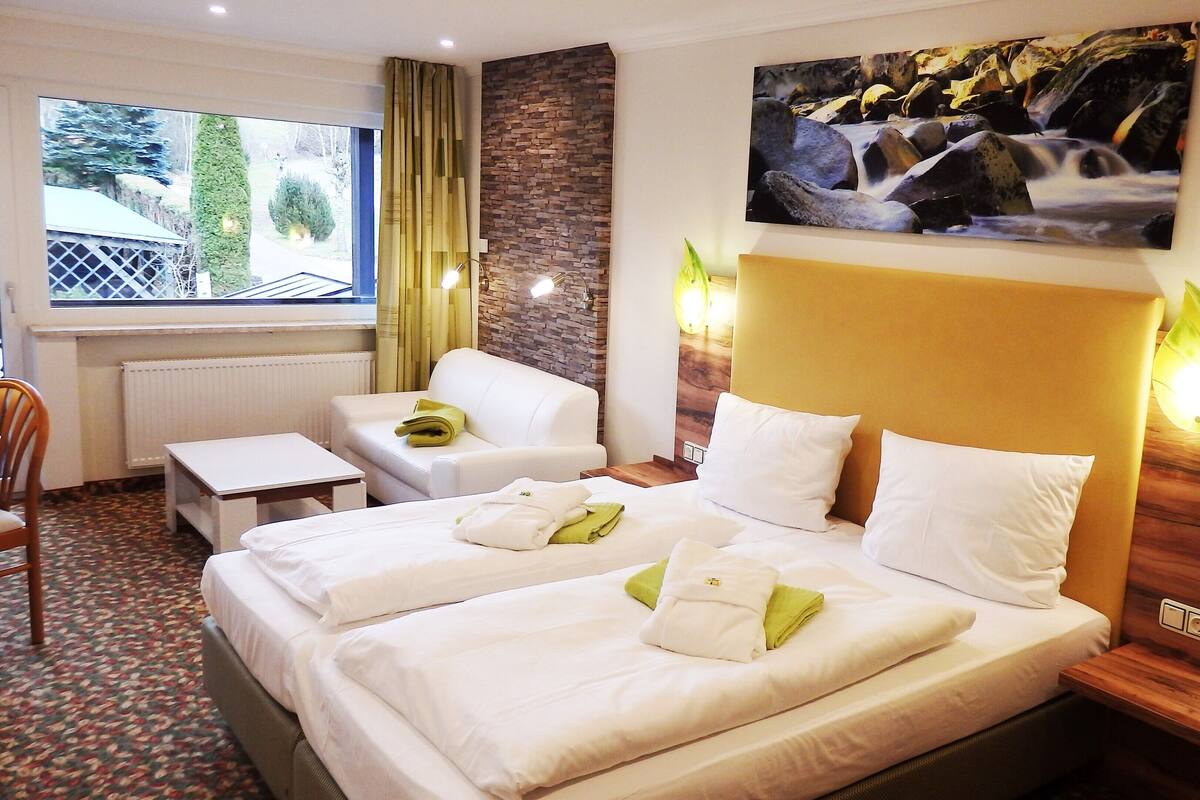 Une chambre d’hôtel avec un lit, deux chaises, une petite table et une fenêtre avec des rideaux.