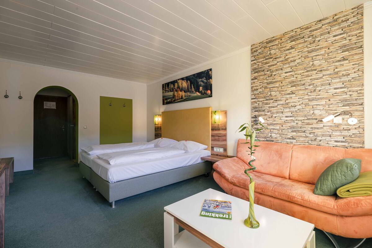 Une chambre d’hôtel avec un lit, un canapé, un tableau au mur et une plante sur la table.