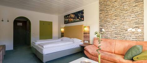 A hotel room with a bed, a sofa, a painting on the wall, and a plant on the table.