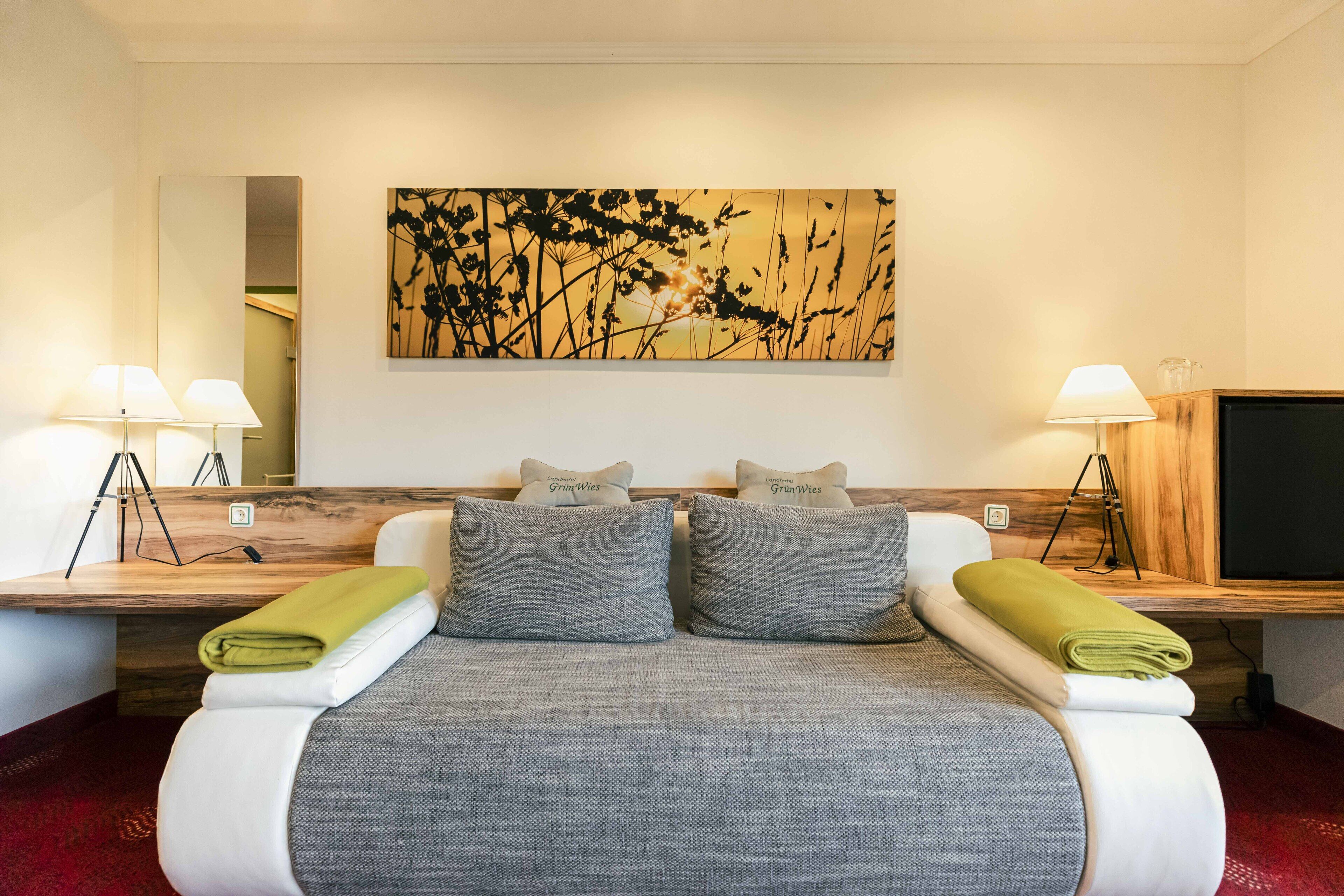 A hotel room with a bed, two bedside lamps, a flat-screen TV, and a painting on the wall.