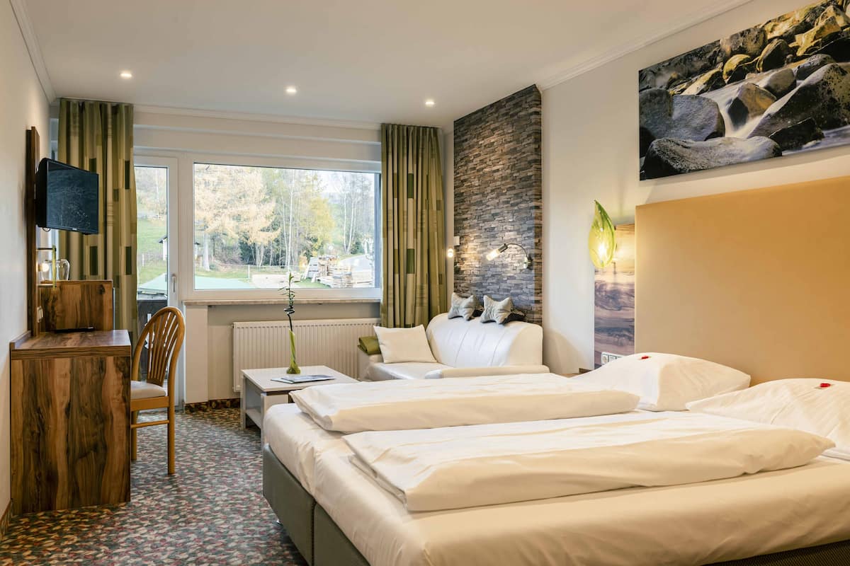 Une chambre d’hôtel avec deux lits, un bureau, une chaise, une télévision et une fenêtre avec des rideaux.