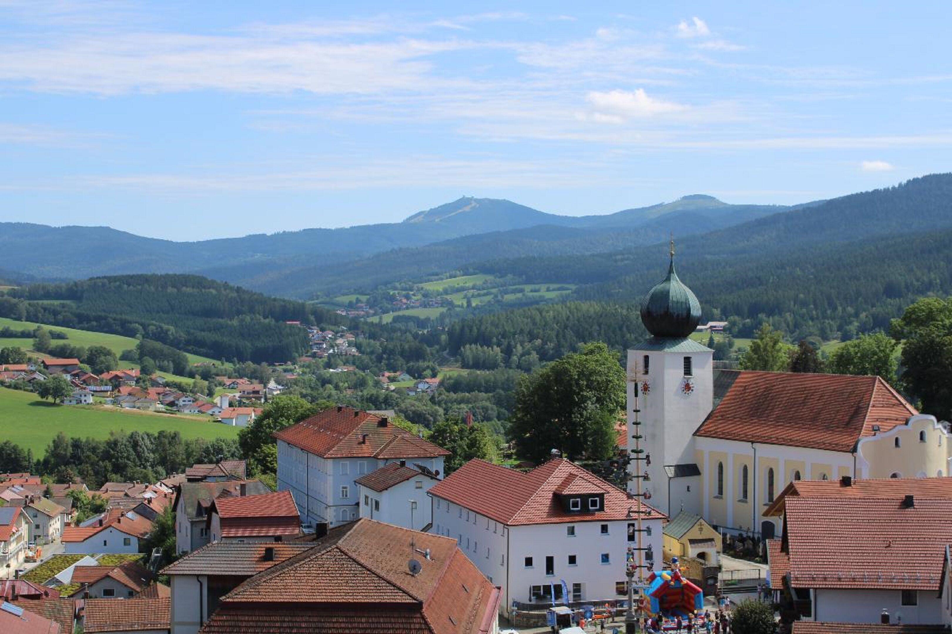 A town with traditional architecture, including a church with a dome and a bell tower, surrounded by green hills and residential buildings.