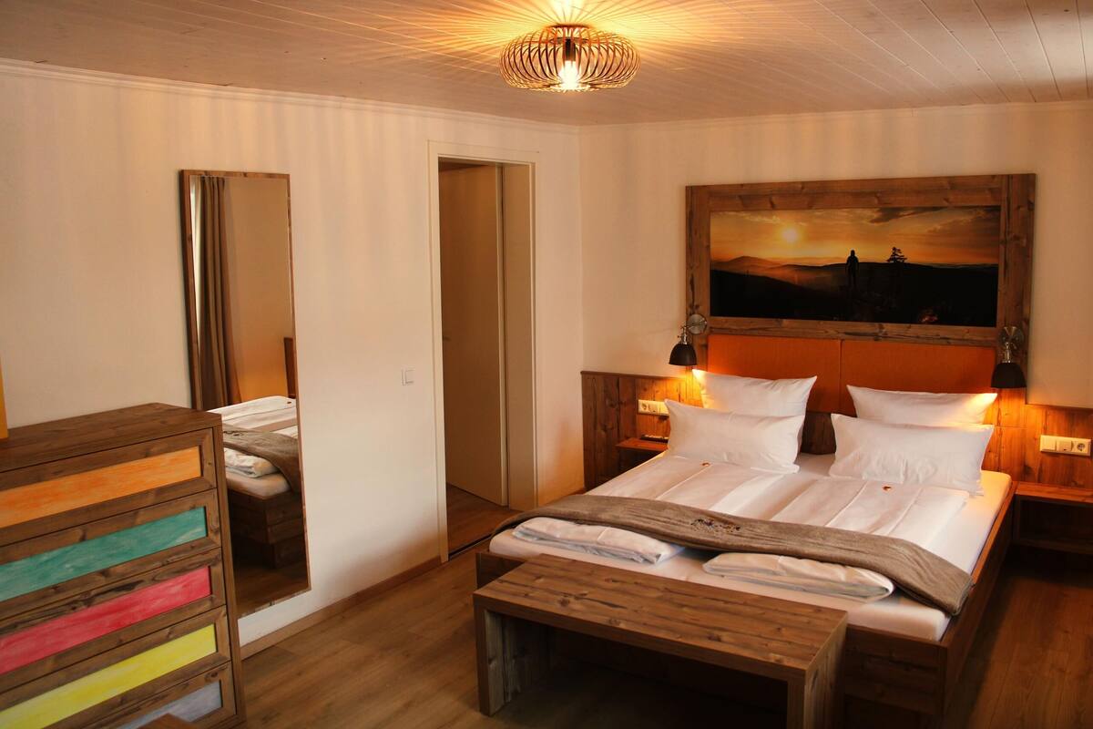 Une chambre à coucher avec un grand lit, une tête de lit en bois, des lampes de chevet, une commode en bois et un miroir.