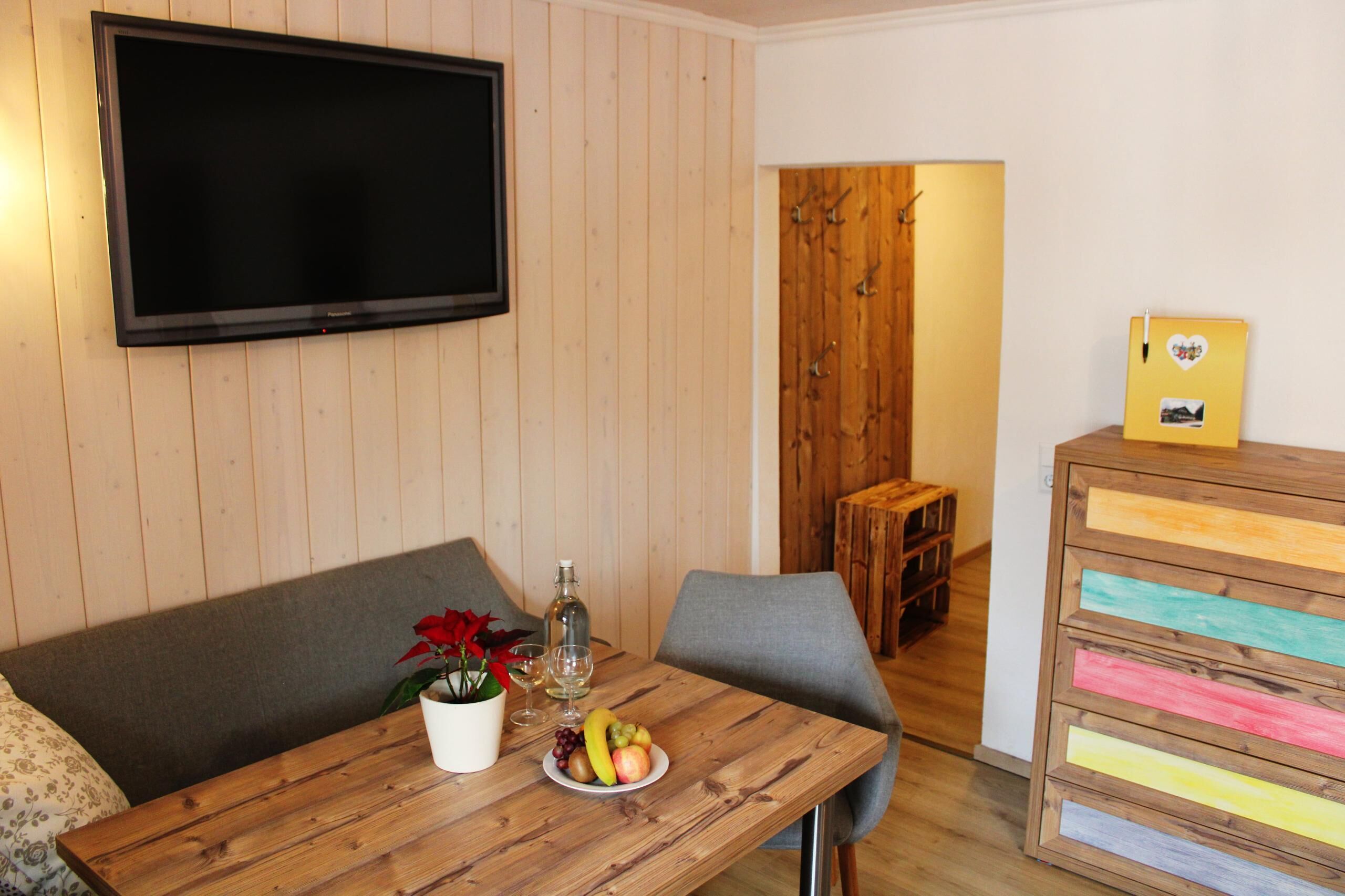 Ett rum med träpanel på väggarna, en platt-tv monterad på väggen, ett träbord med en frukttallrik, en flaska och en krukväxt.