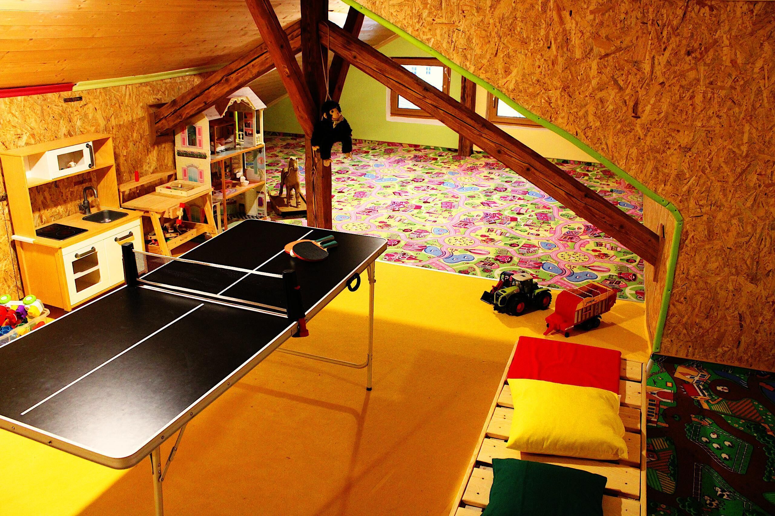 Una sala de juegos con mesa de ping pong, juguetes y un suelo colorido.