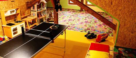 Una sala de juegos con mesa de ping pong, juguetes y un suelo colorido.