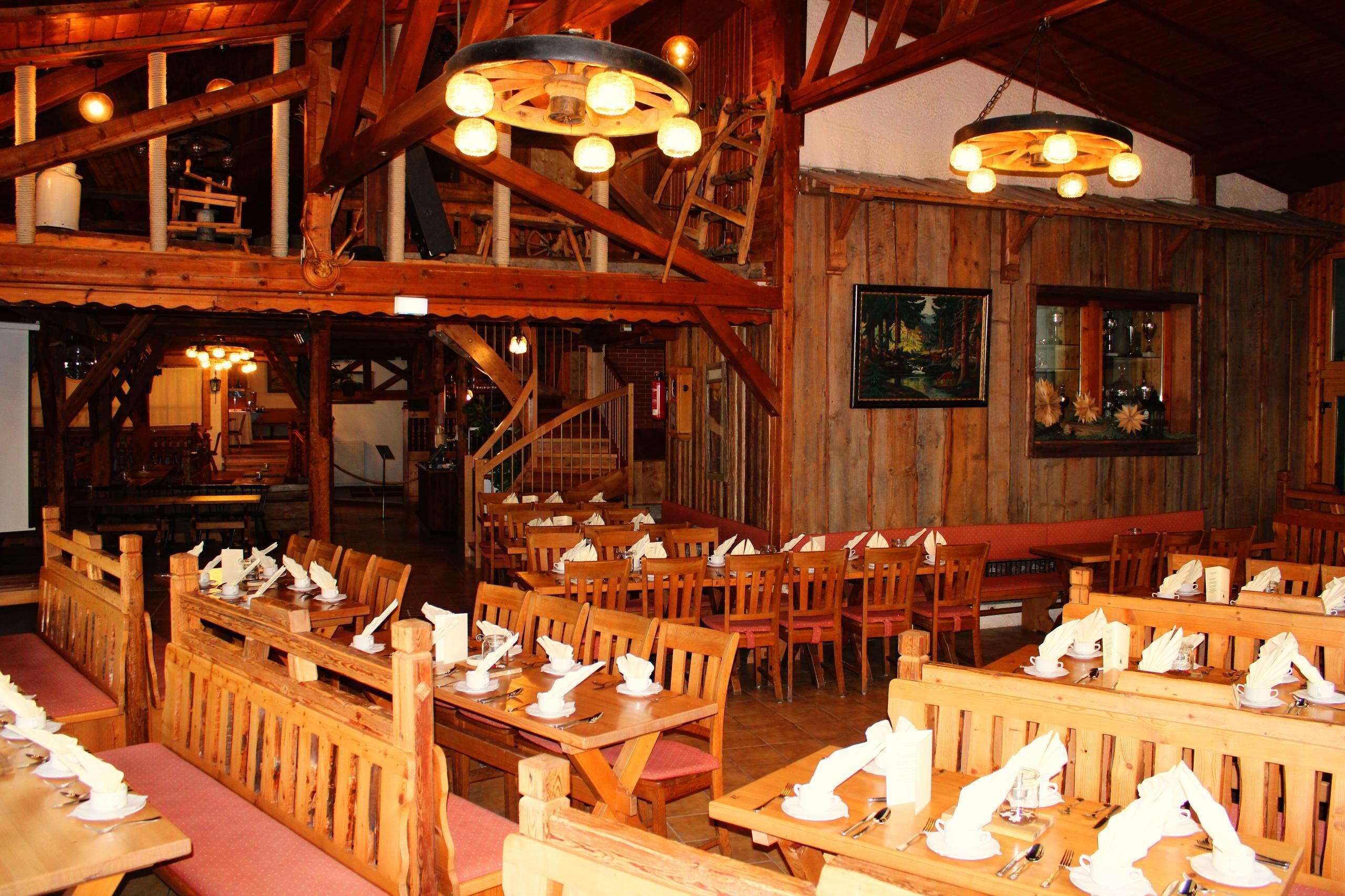 Un interior rústico de madera con varias mesas y bancos para comer, vigas de madera y una escalera.