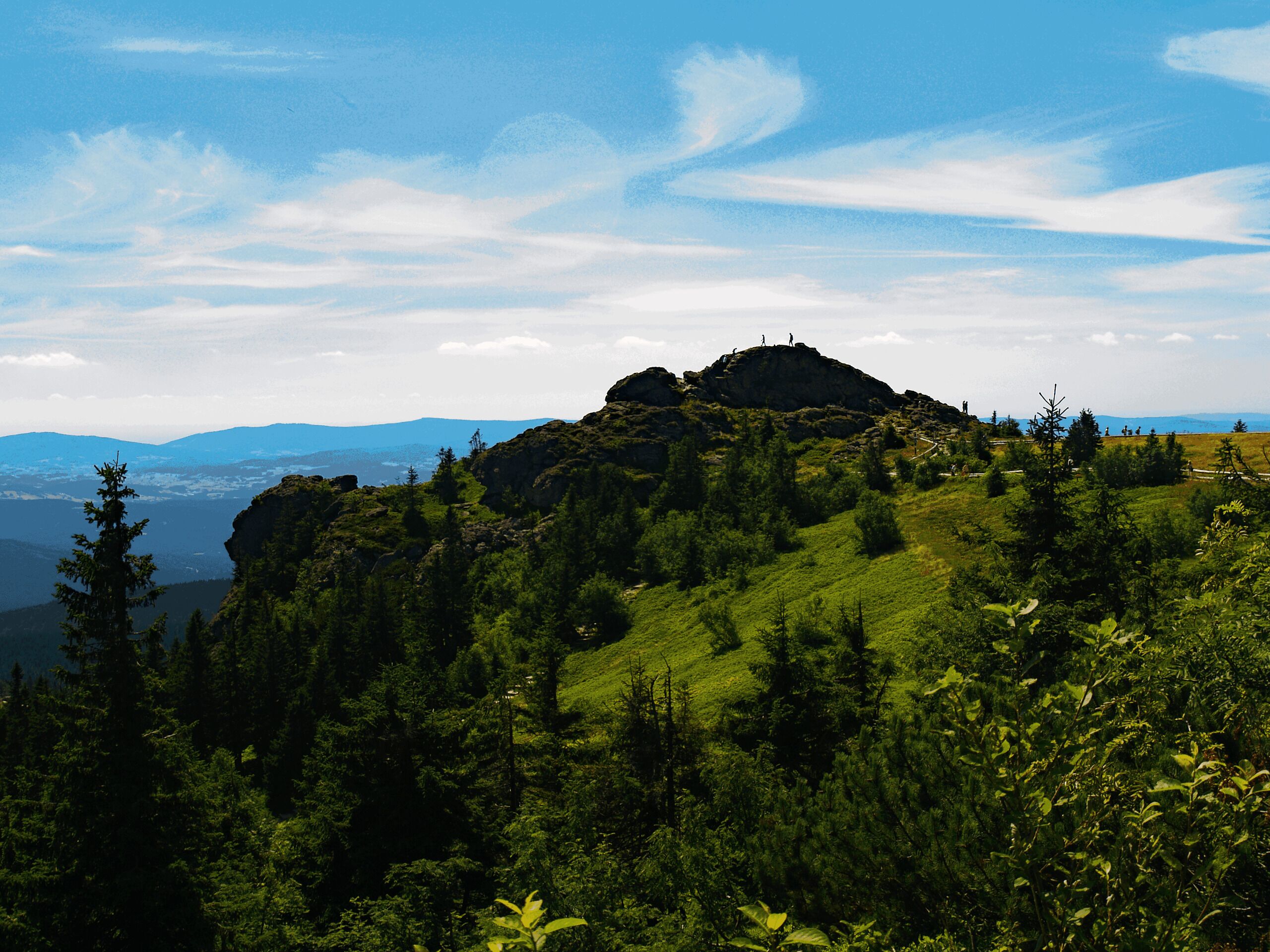 A mountainous landscape with a prominent rocky peak, dense forest, and a clear sky.