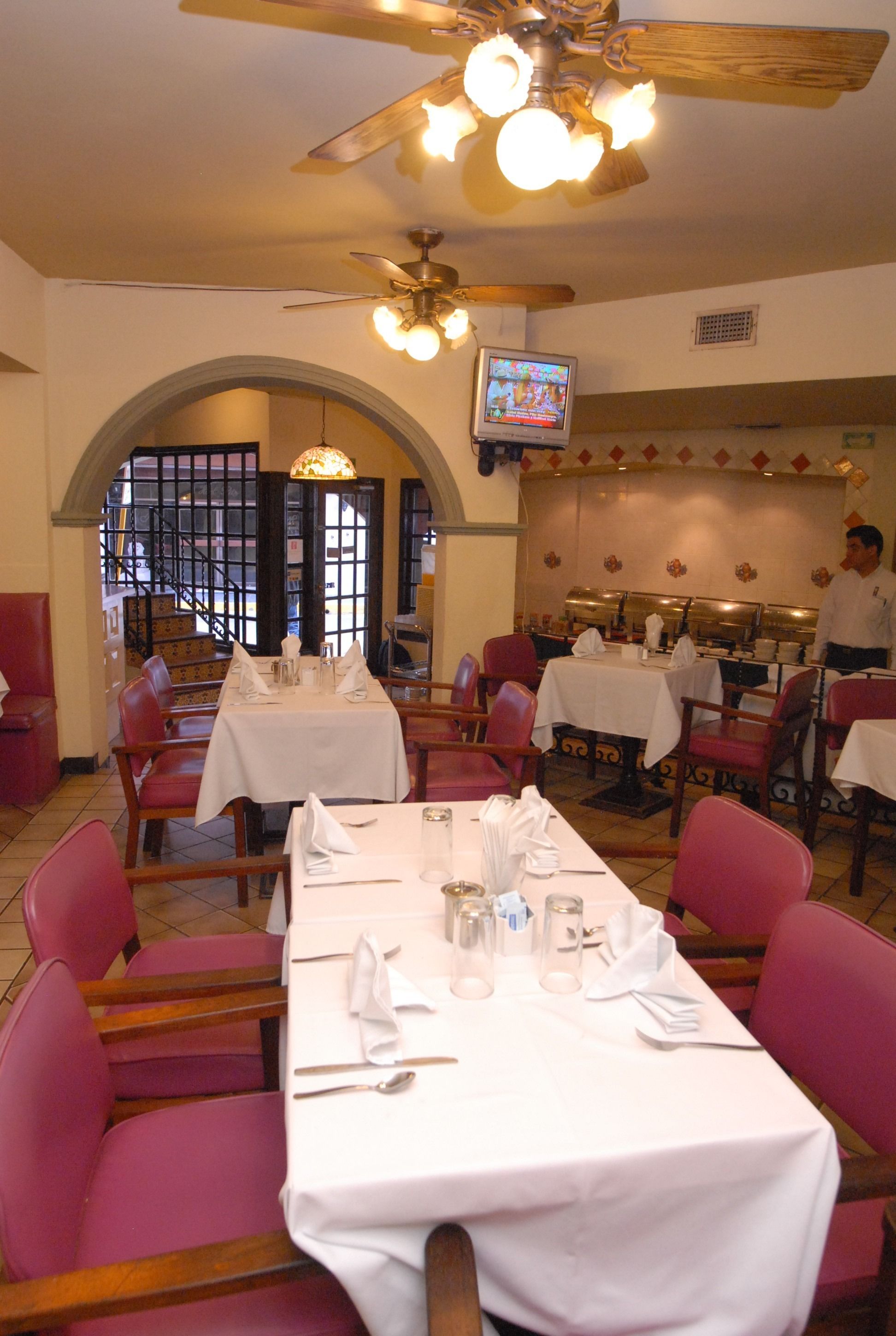 A restaurant with tables set for dining, a television screen, and a chef in the background.