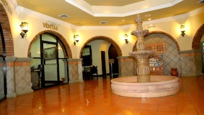 A lobby with a fountain, tiled flooring, and arched doorways.