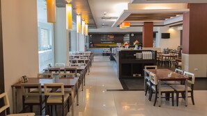 A modern restaurant with long tables and chairs, a bar area, and a view of the outside. - City Park Hotel (Nakhon Ratchasima)