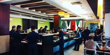 Zona de bufé con varias estaciones de servicio, un árbol de Navidad y un grupo de personas cenando.