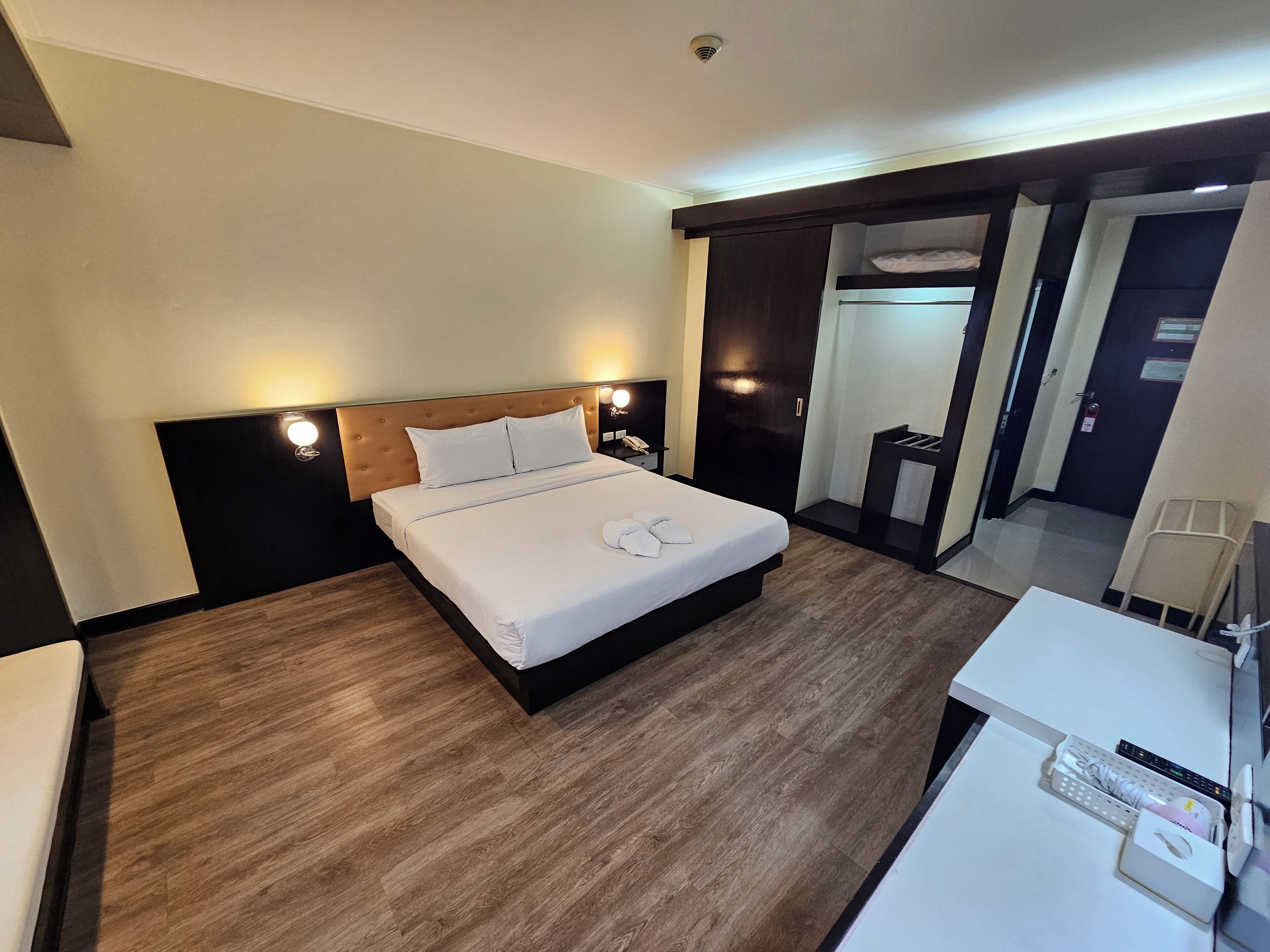 Une chambre d’hôtel avec un grand lit, des tables de chevet, un bureau avec une chaise, un miroir et une armoire.