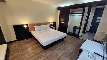 Habitación de hotel con una cama grande, mesitas de noche, un escritorio con silla, un espejo y un armario.