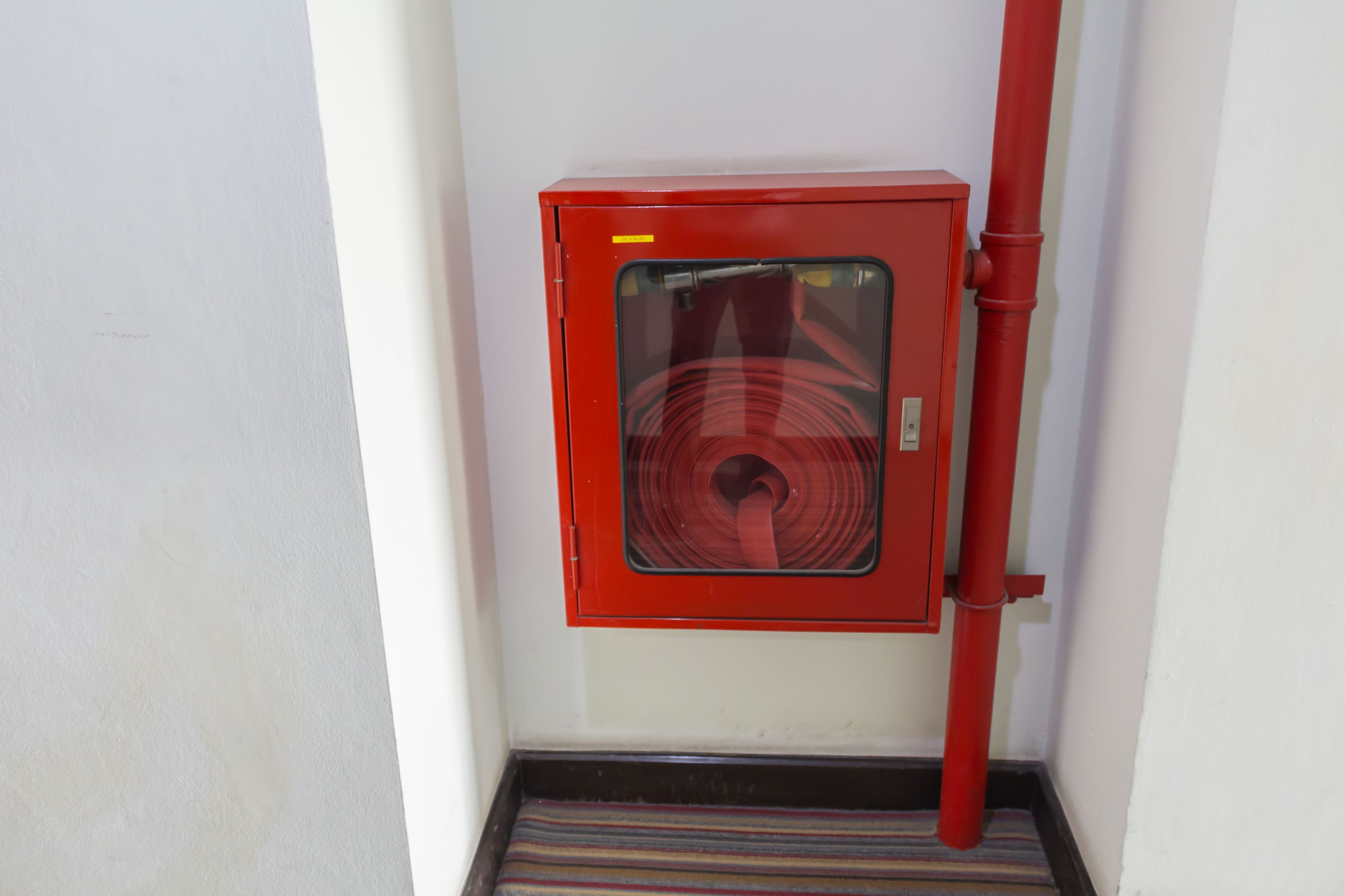 A red electrical box mounted on a wall next to a white pipe.