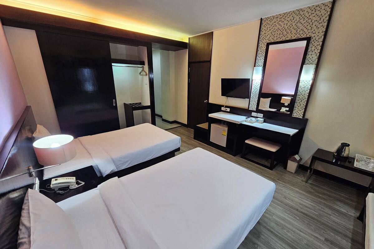 A hotel room with two beds, a desk, a TV, a small fridge, and a mirror.