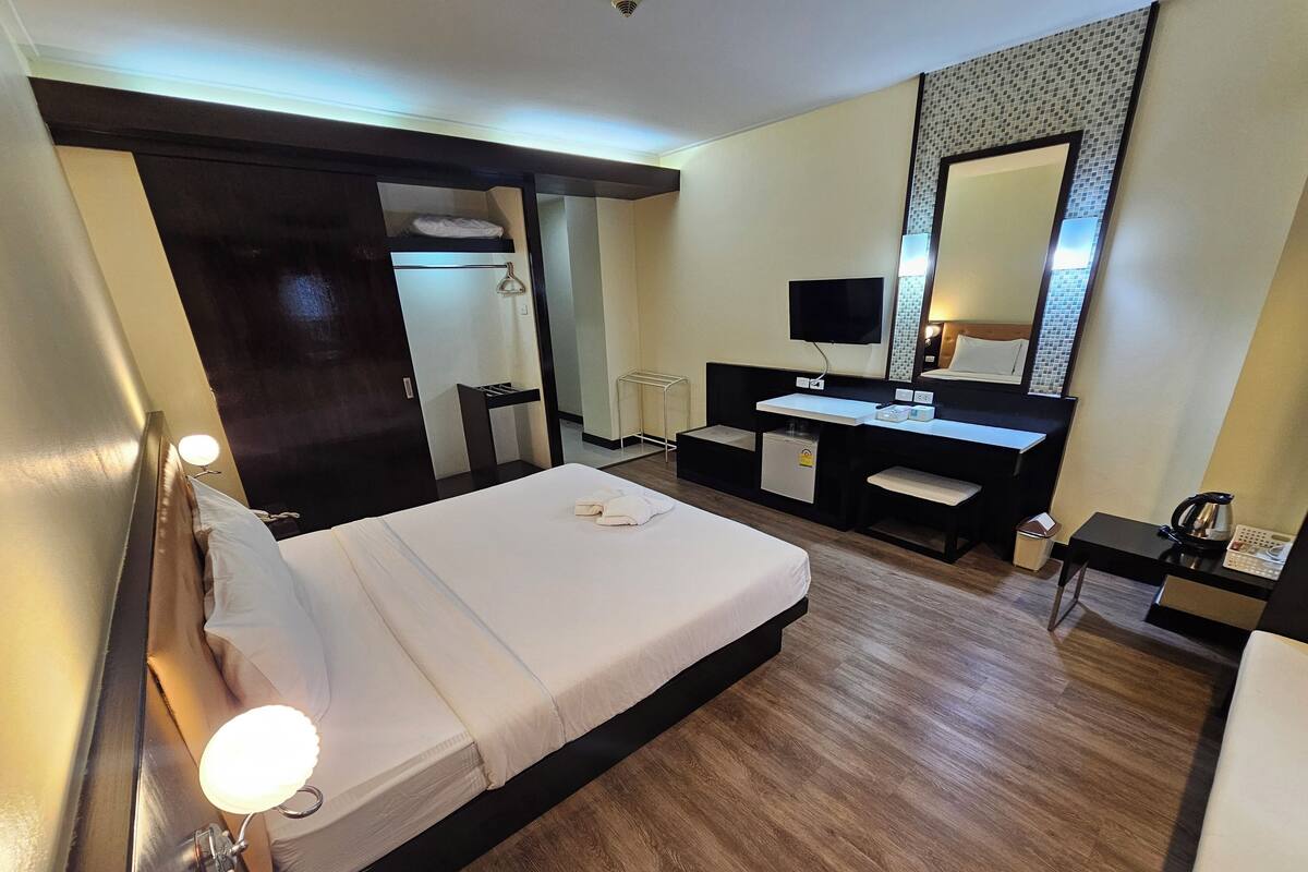 A hotel room with a bed, bedside table, desk, chair, and a large mirror.