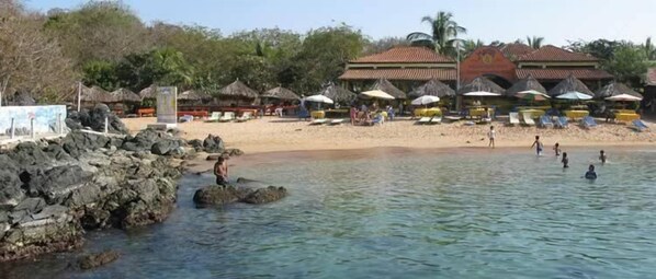A beach with thatched-roof huts, a rocky shoreline, and people swimming and relaxing. - Casa Ixtapa-Zihuatanejo (Zihuatanejo)