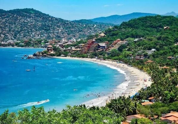 Un pueblo costero con playa, casas y montañas al fondo.