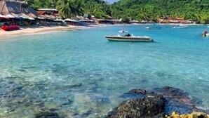 Une plage tropicale aux eaux cristallines, un bateau et un bâtiment à toit de chaume.