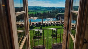 Un balcón con vistas a una piscina, mobiliario exterior y una zona ajardinada.