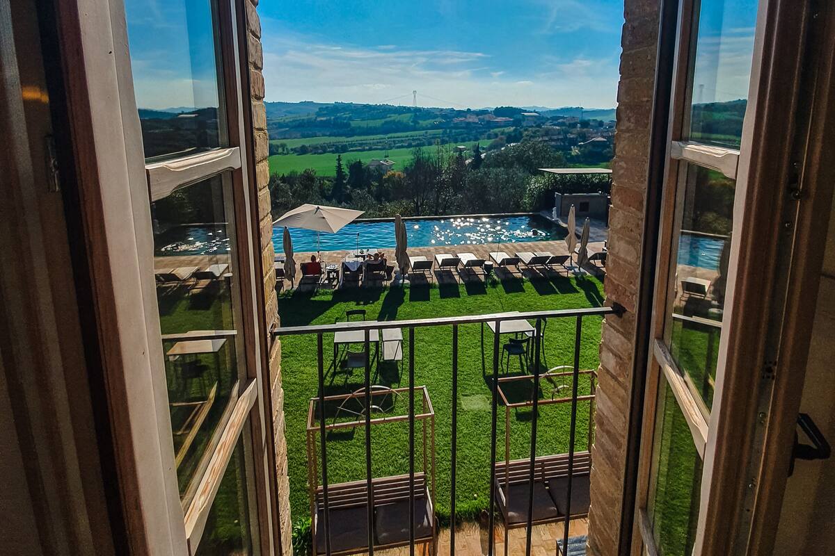 A balcony with a view of a swimming pool, outdoor seating, and a grassy area.