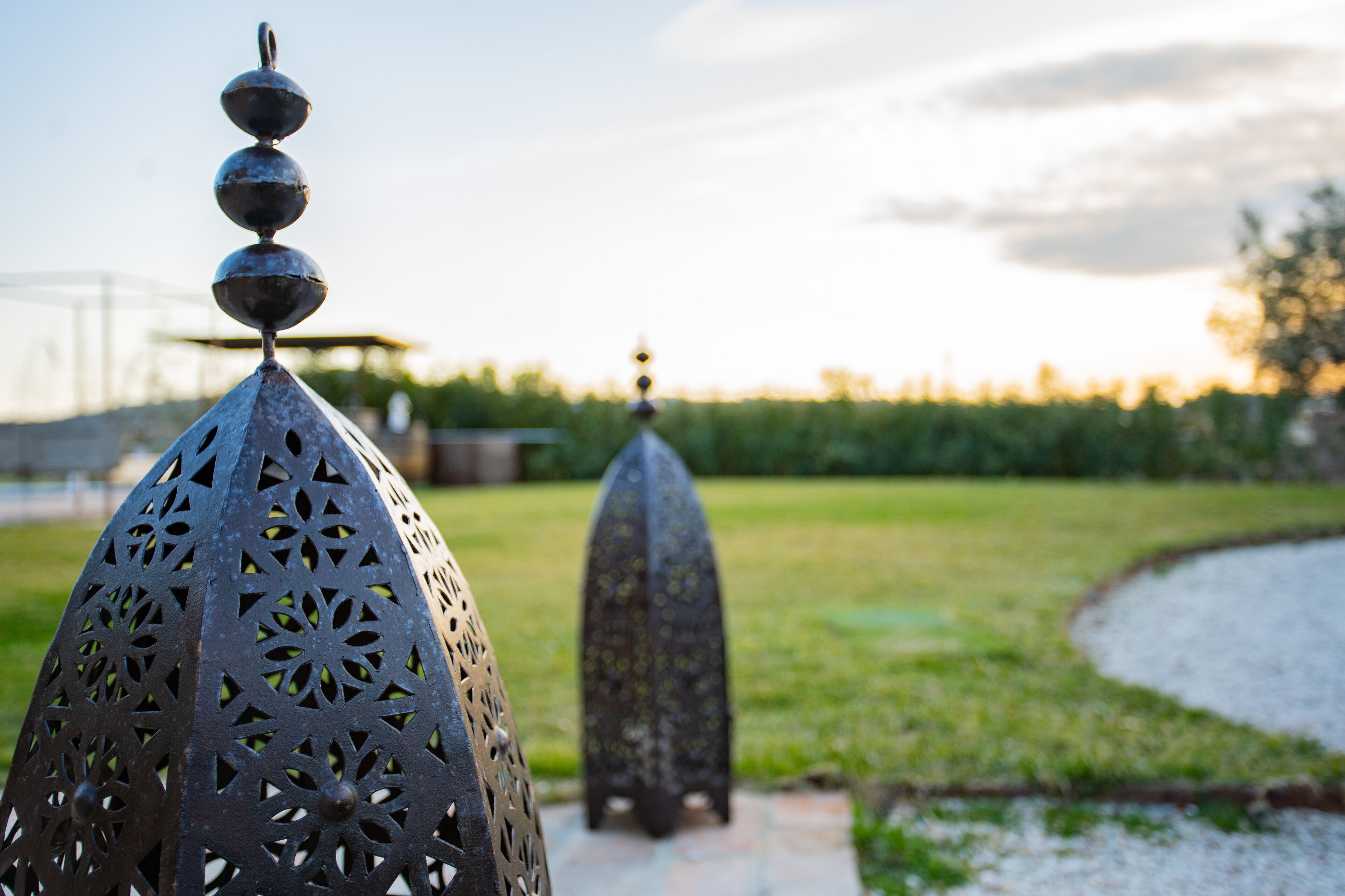 Une structure métallique aux motifs complexes, découpés avec précision, surmontée d’une sphère, et installée dans un jardin aménagé sous un ciel dégagé.