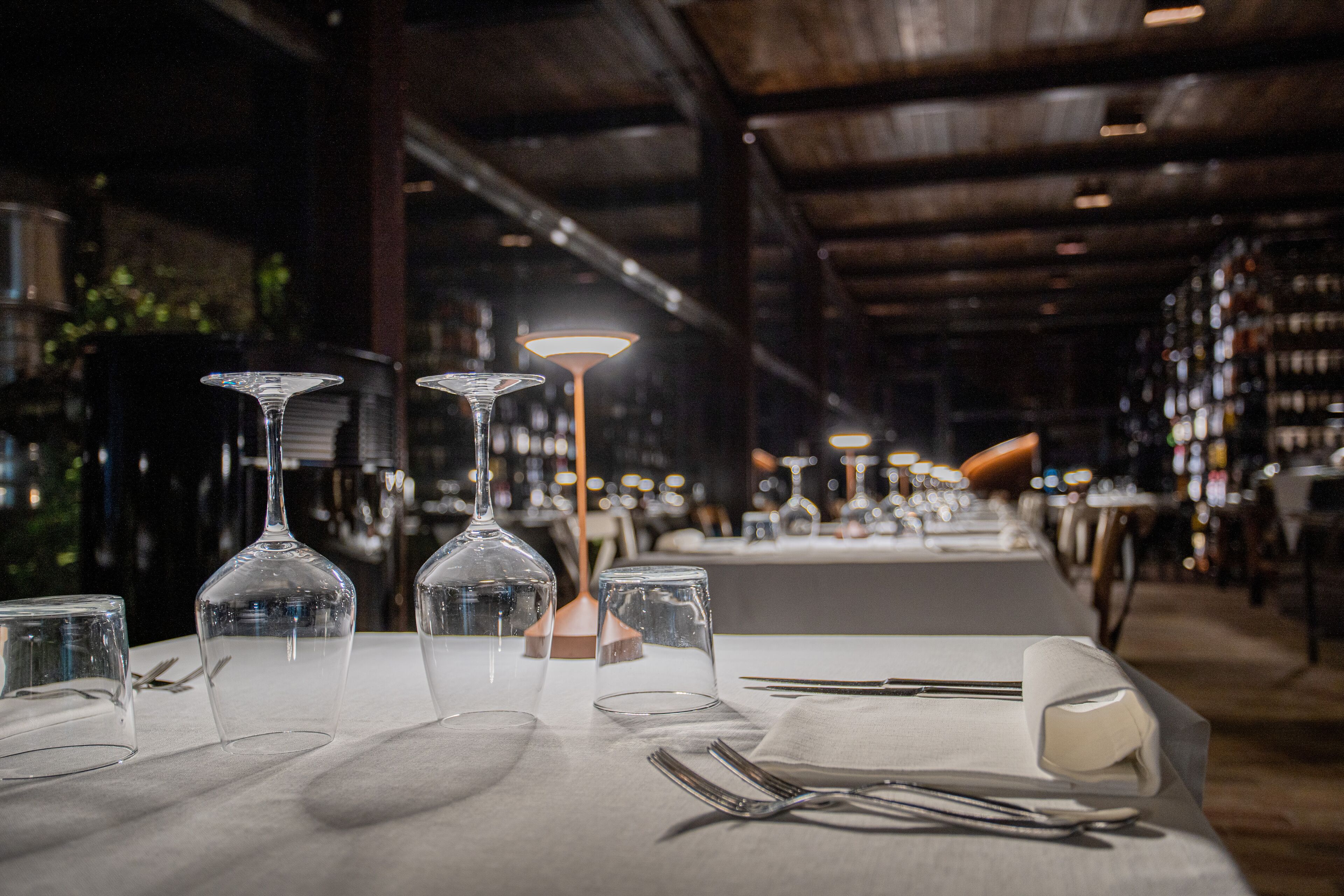 A restaurant interior with tables set for dining, featuring wine glasses and cutlery.