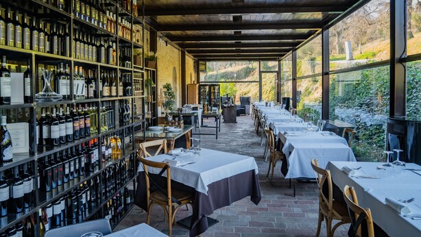 Un restaurante con una bodega de vinos, mesas dispuestas para comer y vistas al exterior.