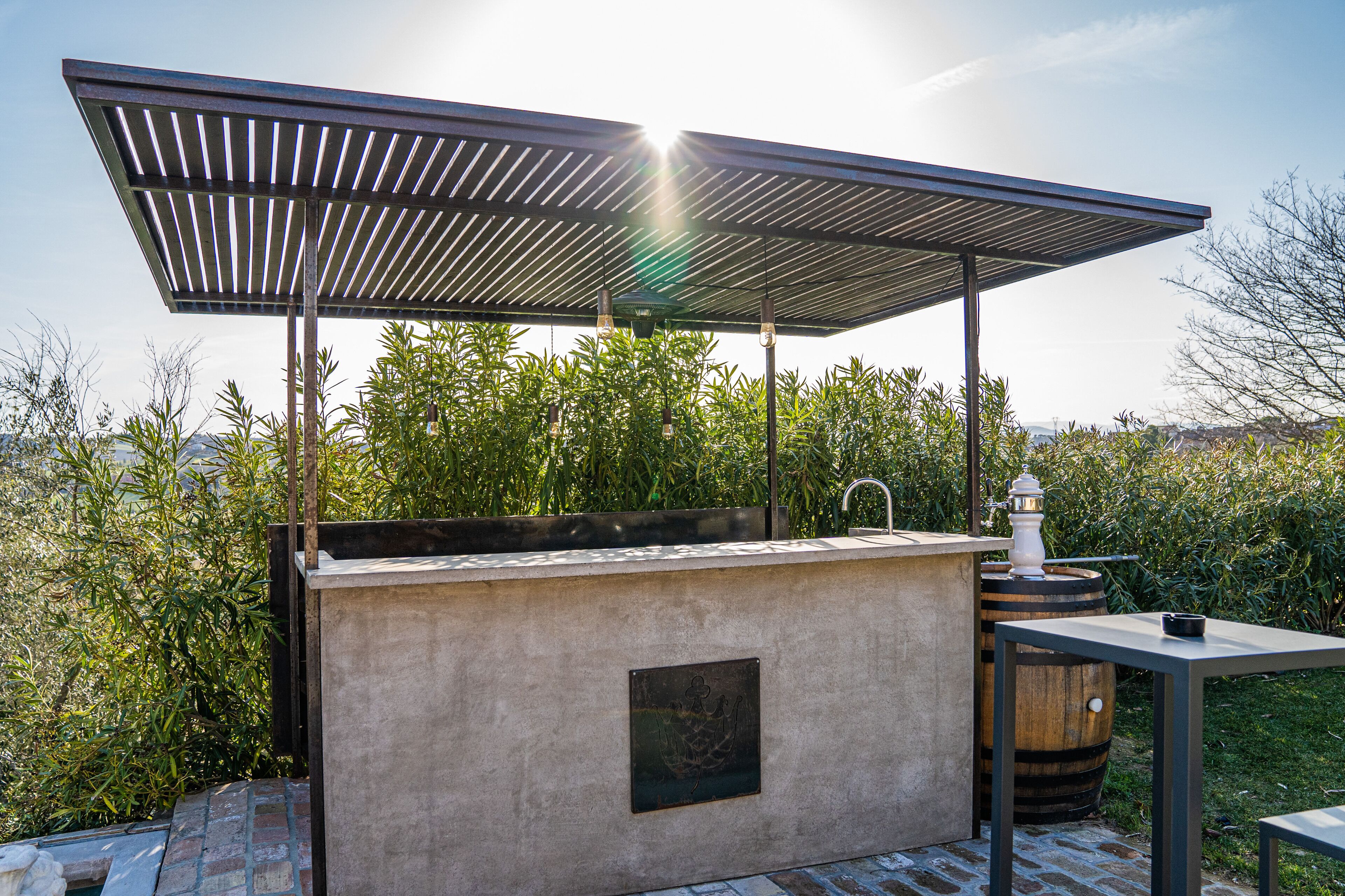 Un patio exterior con una parrilla incorporada, un barril de madera y una mesa de metal.