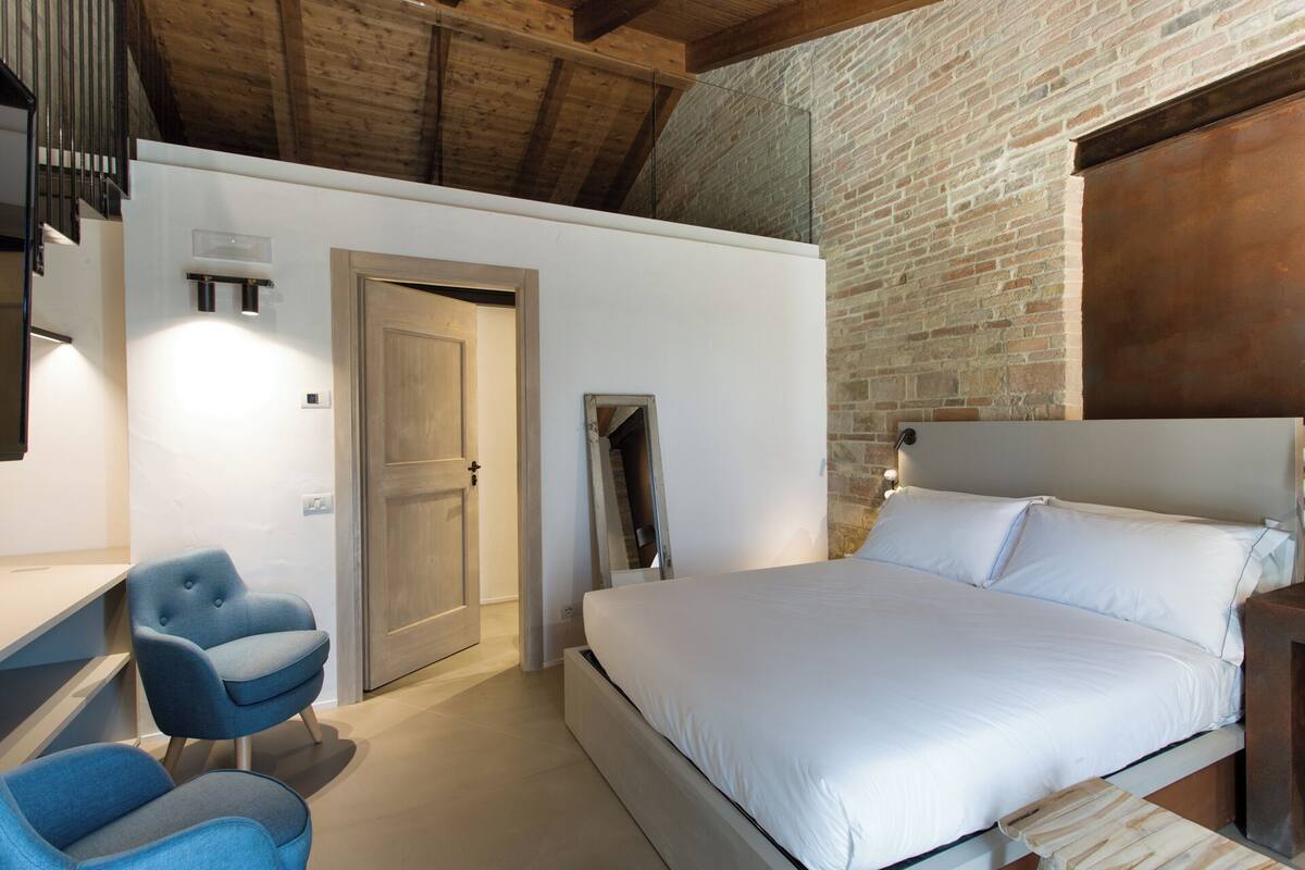 A bedroom with a bed, a chair, a desk, and a mirror.